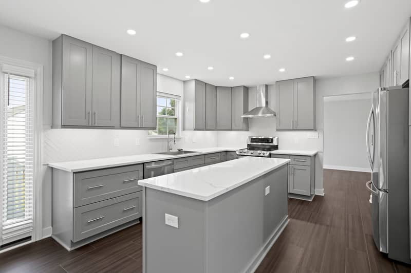 Renovated kitchen with gray shaker cabinetry, white quartz counters, herringbone tile backsplash, center island, stainless range with vent hood and refrigerator
