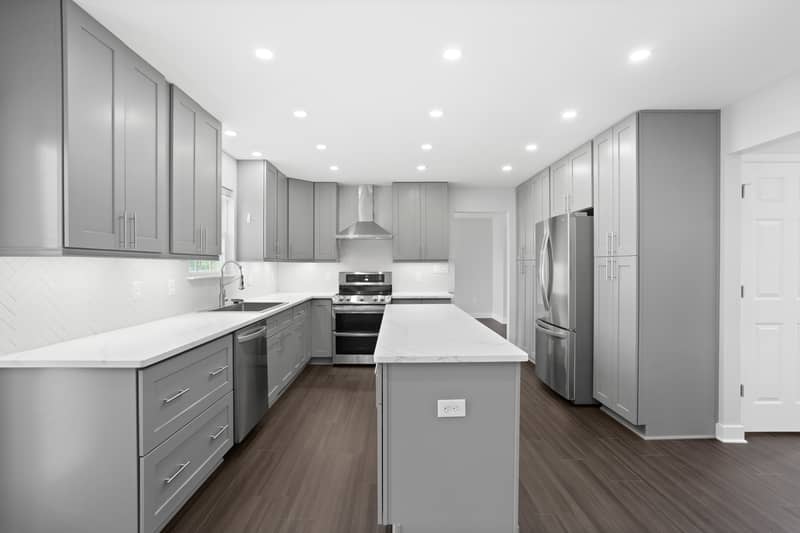 Open kitchen with gray cabinets, quartz island, stainless range and refrigerator, and a built-in coffee bar with open shelving and herringbone tile