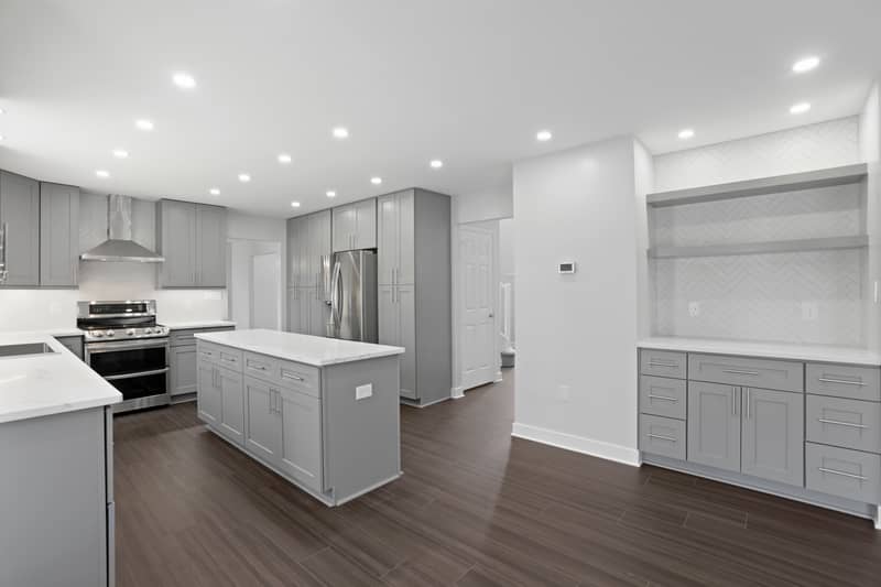 Close view of kitchen cooking area with stainless double-oven range, chimney vent hood, white herringbone tile backsplash, gray cabinets and quartz counters