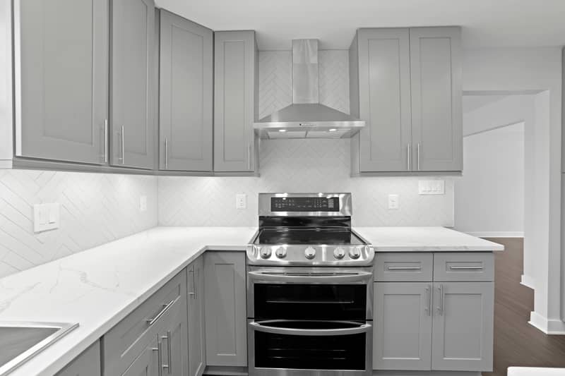 Kitchen sink area with stainless single-basin sink and pull-down faucet beneath a window, white herringbone backsplash and quartz counters between gray cabinets