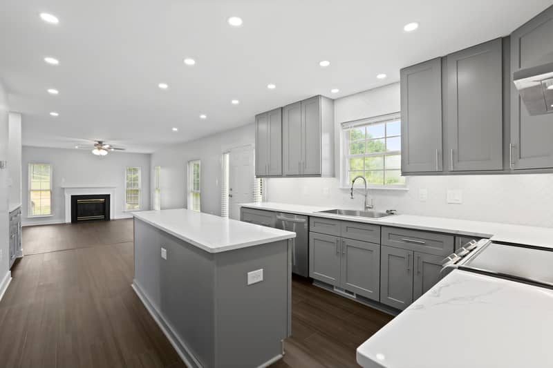 Kitchen with gray cabinets, white quartz island and counters, stainless range and dishwasher, herringbone backsplash, recessed lighting and dark LVP floors
