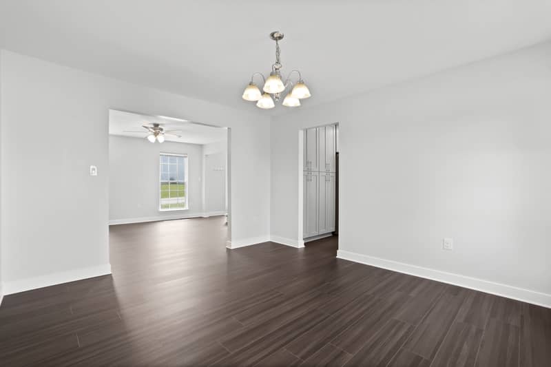 Dining room with chandelier and dark LVP flooring opening to the family room beyond, with tall gray pantry cabinetry to the right