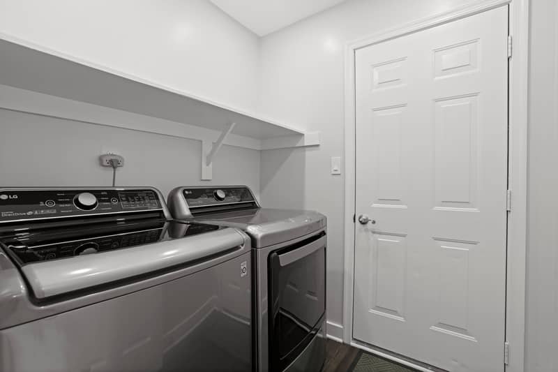 Laundry room with side-by-side stainless LG top-load washer and dryer, a wall shelf above, and a white six-panel door