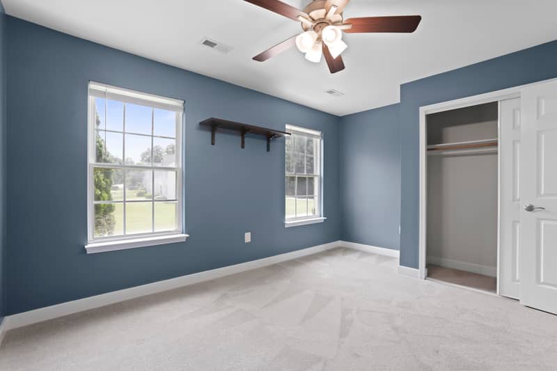 Slate-blue carpeted bedroom with a lighted ceiling fan, a closet with bypass door, and an open door to the upstairs landing