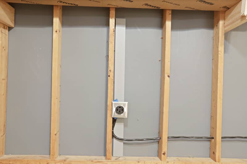 Close-up of a 240-volt NEMA outlet mounted on an exposed framed garage wall with conduit and wiring, indicating EV-charging readiness