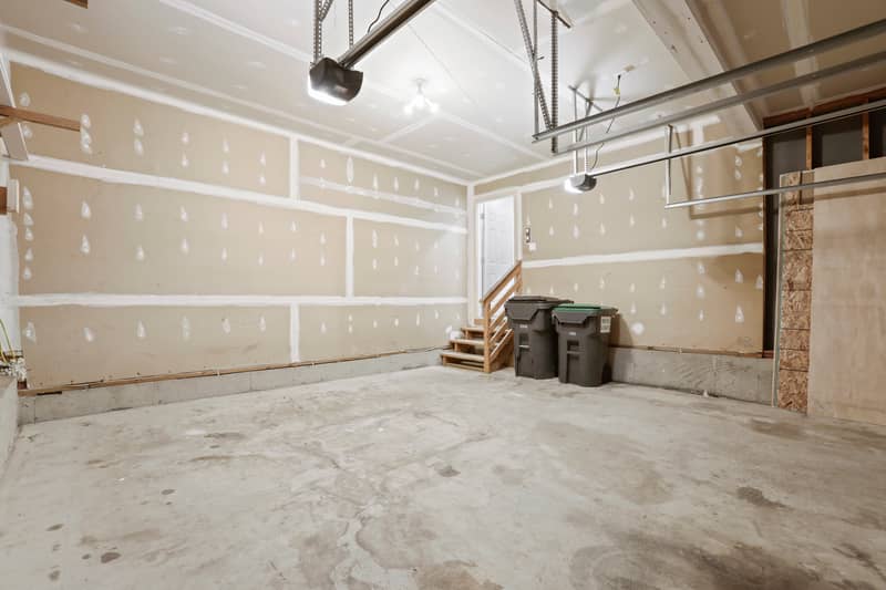 Two-car garage interior with drywalled walls, concrete floor, two ceiling-mounted door openers, and wood steps leading up to the interior house entry door